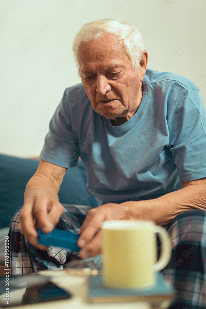 Senior Man Sitting On Bed At Home Taking Medication Senior Man Sitting On Bed At Home Taking Medication