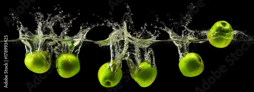 Green apple falling in water on black background