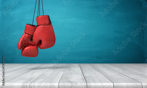 3d rendering of two red boxing gloves hanging above a wooden desk in front of a blue blackboard background. © gearstd