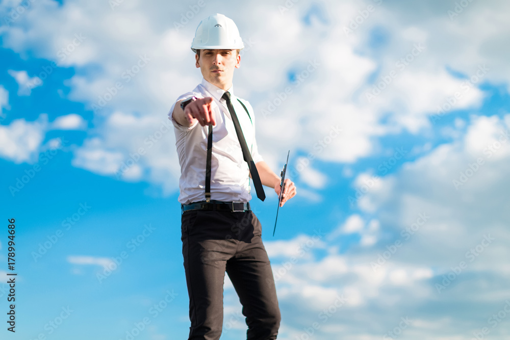 Young attractive foreman in white helmet, tie and braces stand on the roof with tablet Young attractive foreman in white helmet, tie and braces stand on the roof with tablet