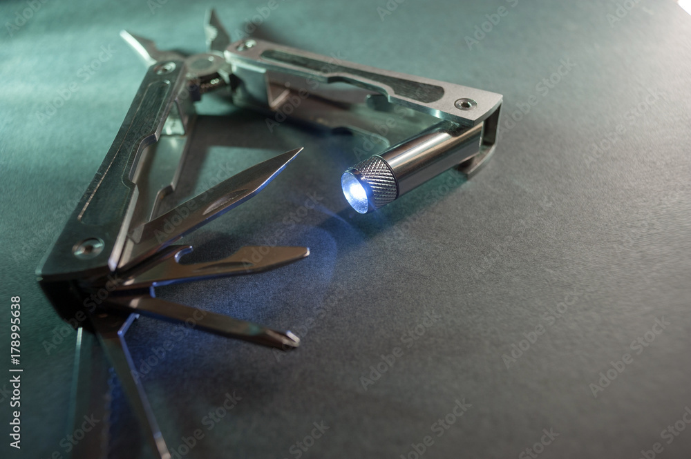 Combined pliers, multifunctional, with flashlight. Against the background of a gray texture Combined pliers, multifunctional, with flashlight. Against the background of a gray texture