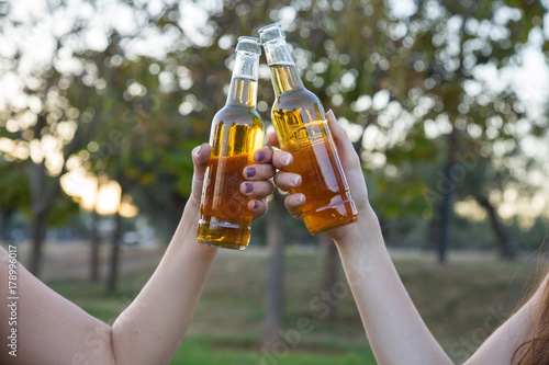 Close-up of two young women toasting with beer bottles having fun. 