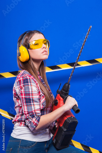 Pretty sexy worker girl in chechered shirt, build goggles and jeans stand with drill photo