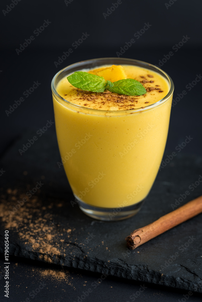Fresh mango smoothie with cinnamon on a black slate background. Fresh mango smoothie with cinnamon on a black slate background.