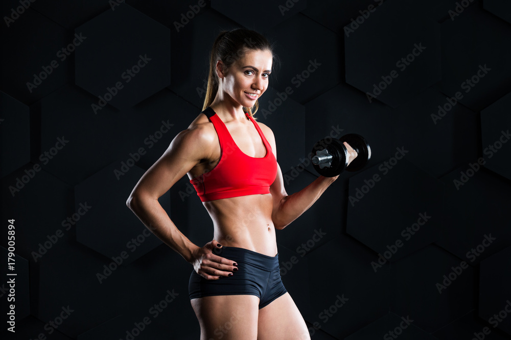 Fototapeta premium Beautiful woman doing a fitness workout with weights on a dark background.
