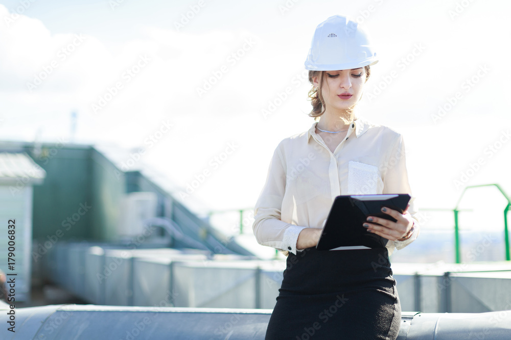 Attractive businesslady in white blouse, watch, helmet and black skirt stand on the roof and hold tablet Attractive businesslady in white blouse, watch, helmet and black skirt stand on the roof and hold tablet