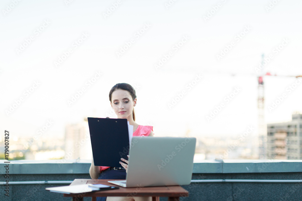 Attractive businesslady in pink blouse sit on the roof and work with laptop Attractive businesslady in pink blouse sit on the roof and work with laptop