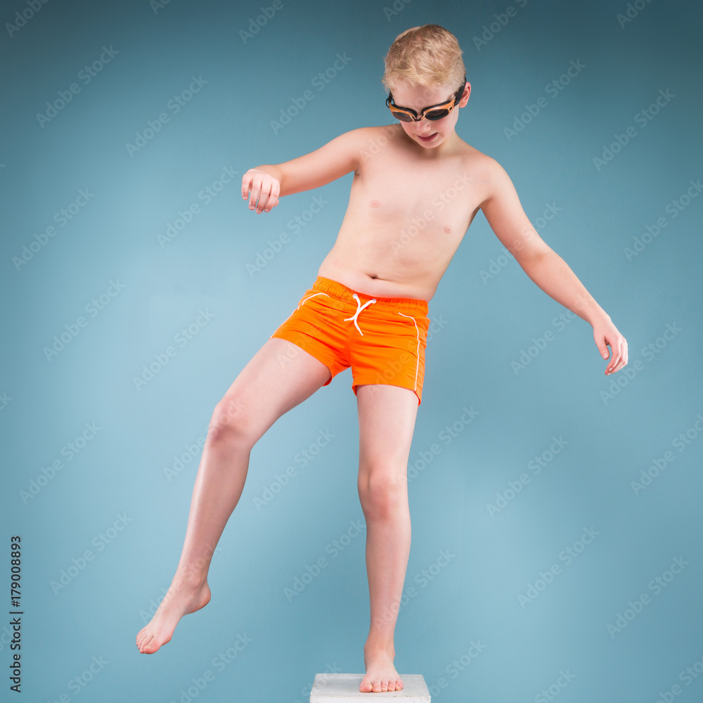 Teenage boy in orange shorts and swimming glasses stand on one leg