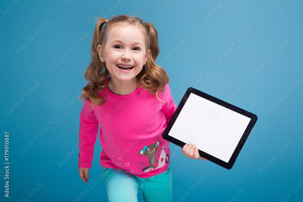 Beautiful little girl in pink shirt with monkey and blue trousers hold empty tablet Beautiful little girl in pink shirt with monkey and blue trousers hold empty tablet