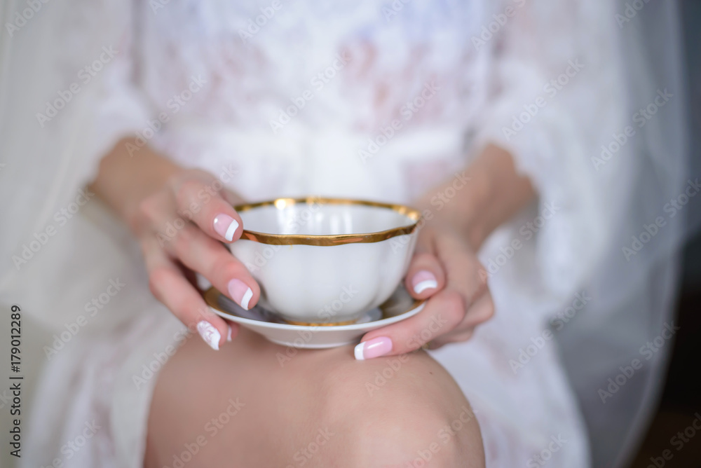 White cup and saucer with tea in the hands of the bride