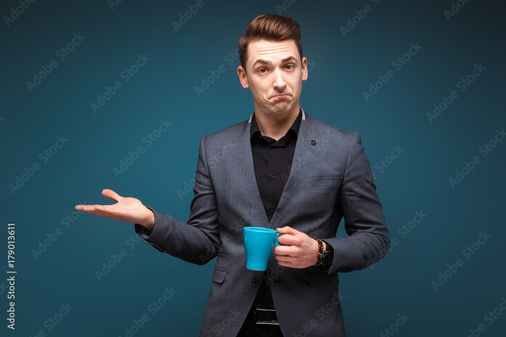 Young attractive businessman in grey jacket and black shirt hold blue cup Young attractive businessman in grey jacket and black shirt hold blue cup
