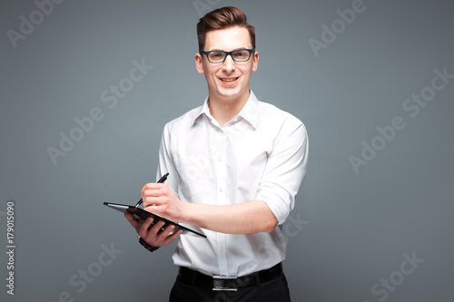 Handsome young businessman in costly watch, black glasses and white shirt hold tablet and pen