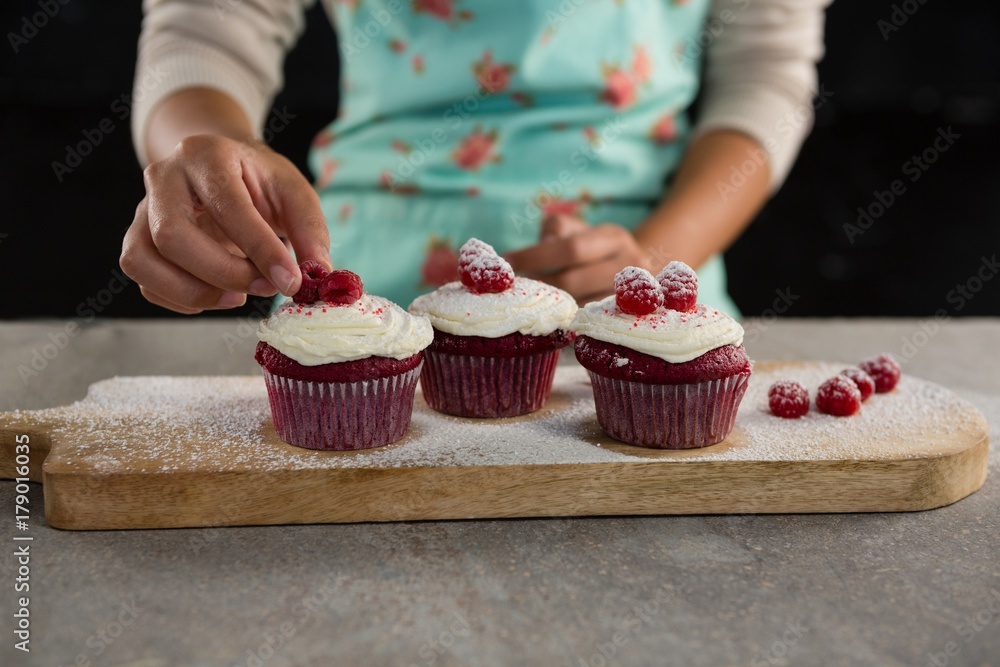 Woman arranging raspberries on cupcakes