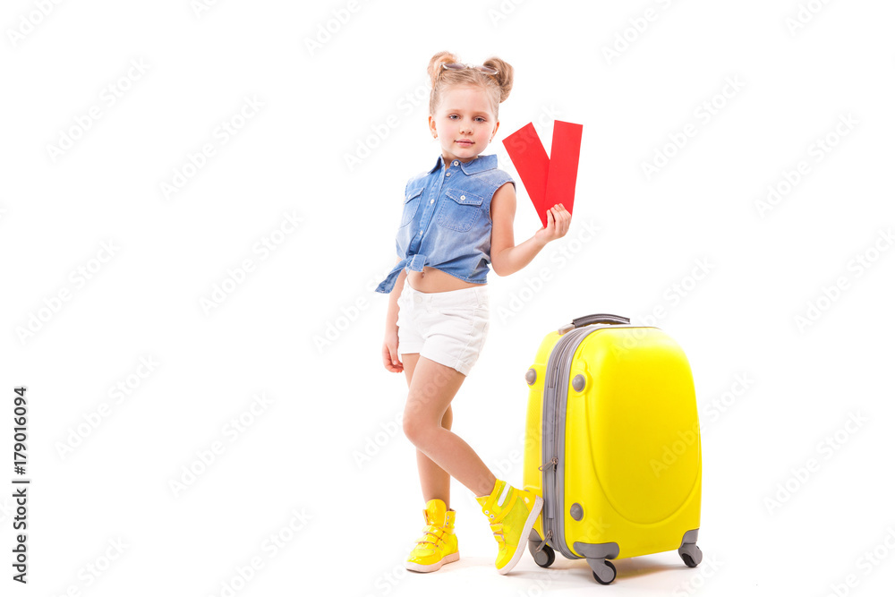 Pretty little girl in blue shirt, white shorts and sunglasses stand near the yellow suitcase and hold red cards Pretty little girl in blue shirt, white shorts and sunglasses stand near the yellow suitcase and hold red cards