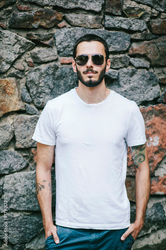 Young man wearing white blank t-shirt with beard in glasses, standing on the street on city background. Street photo © andrew_shots