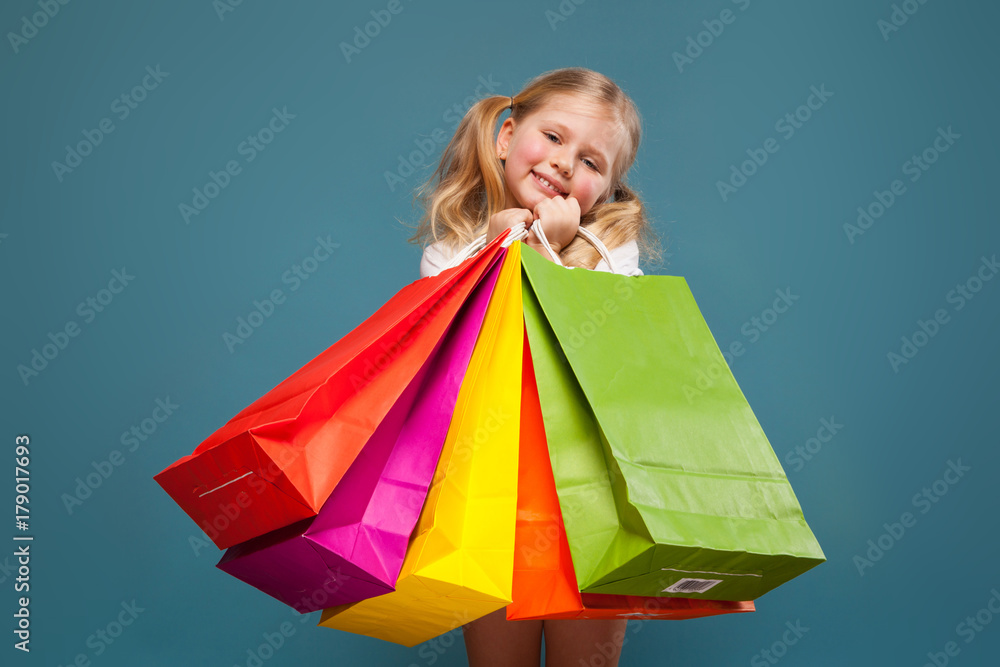 Adorable cute little girl in white shirt, white jacket and white shorts hold colorful paper bags