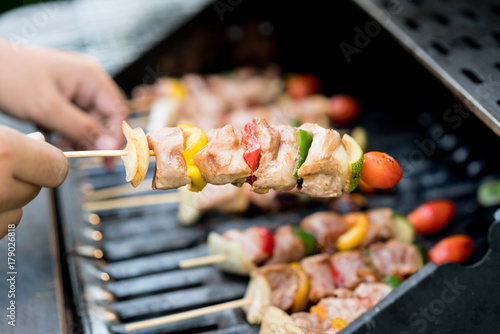 Close up male hand touches barbeque on skewers in grill stove.