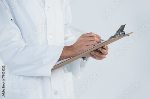 Doctor writing on clipboard against white background