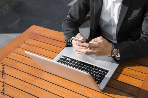 Male businessman or worker in black suit near laptop looking in his phone