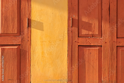 Orange retro thai wooden folding door with yellow wall under evening sunlight © ZUP