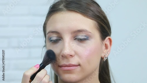 Woman is doing facial cosmetic makeup using face powder rouge brush to a model to create blush cheek.Beauty salon