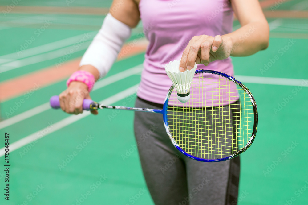 injured woman wearing sportswear  painful arm with gauze bandage  holding shuttlecock and racket playing badminton, focus on shuttlecock.
