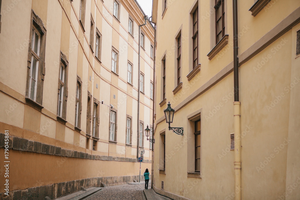 Tourist girl in green jacket walks along beautiful deserted narrow street in Prague between two historic buildings