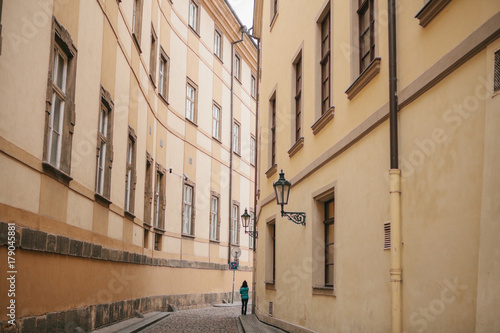 Photography Tourist girl in green jacket walks along beautiful deserted narrow street in Pra