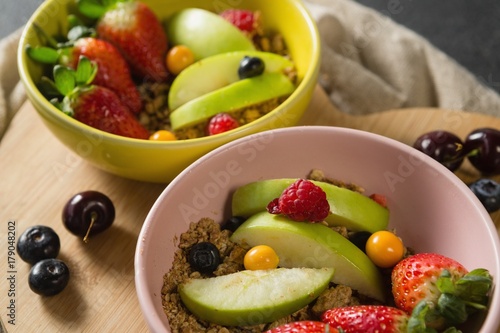 Bowls of breakfast cereals with fruits on chopping board