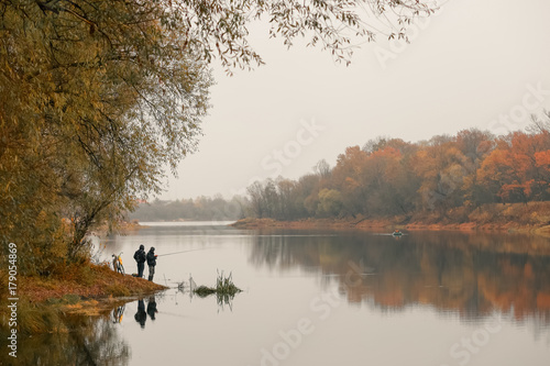 fishermen stand by the water of a forest lake in autumn. photo