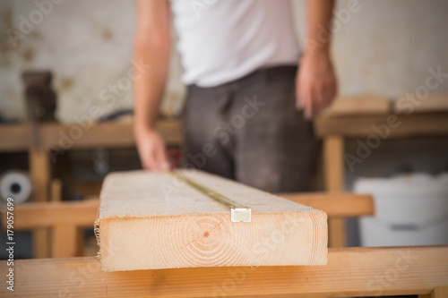Male carpenter working on raw wood / boards / plank. Optical focus is on the foreground.
