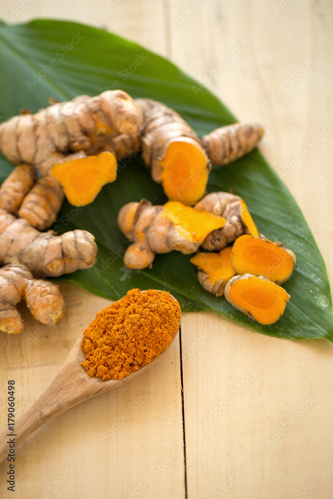 Turmeric powder in a wooden spoon and fresh turmeric on wooden background Turmeric powder in a wooden spoon and fresh turmeric on wooden background