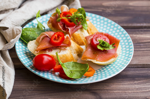 Canapes appetizer with prosciutto ham, pepper slices, tomatoes and green spinach and rucola leaves, healthy crostini or bruschettas italian appetizer seasoned