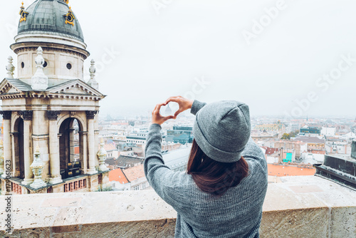 woman shows heart with hands with beautiful view of old european city on background