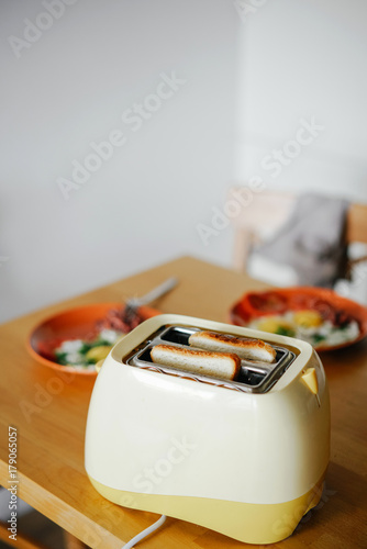 yellow toaster with toasted bread for breakfast inside, on the table in the kitchen interior. photo