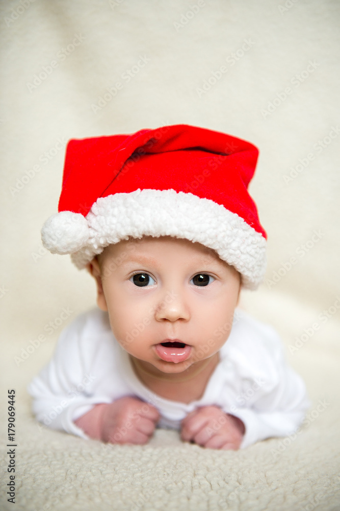 Little baby in red cap of Santa Claus celebrates Christmas. Christmas photo of infant in red cap. New Year's holidays and Christmas tree. Little baby in red cap of Santa Claus celebrates Christmas. Christmas photo of infant in red cap. New Year's holidays and Christmas tree.