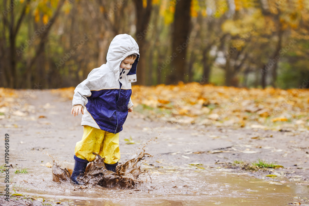 Happy child jumping on puddles in rubber boots Happy child jumping on puddles in rubber boots