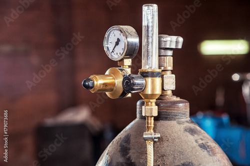 Close-up of a metal gas cylinder with a reducer and a pressure sensor in the background industrial workshop photo