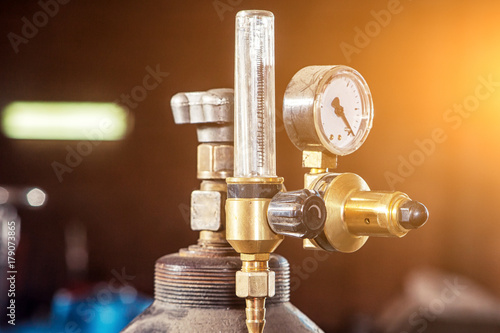 Close-up of a metal gas cylinder with a reducer and a pressure sensor in the background industrial workshop photo