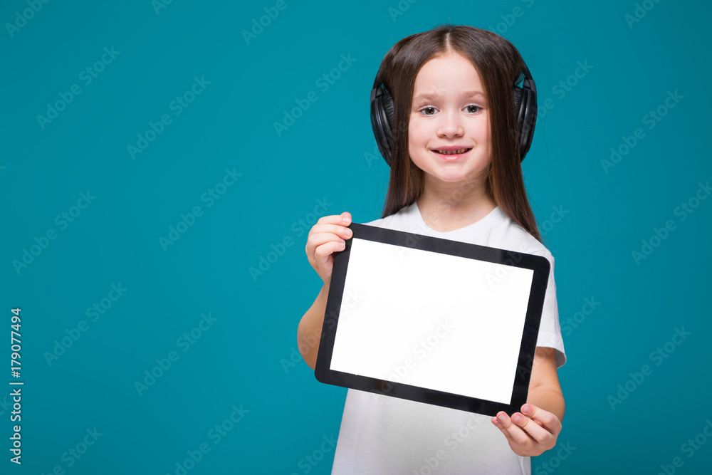 Beauty little girl in tee shirt and earphones with long hair hold tablet Beauty little girl in tee shirt and earphones with long hair hold tablet