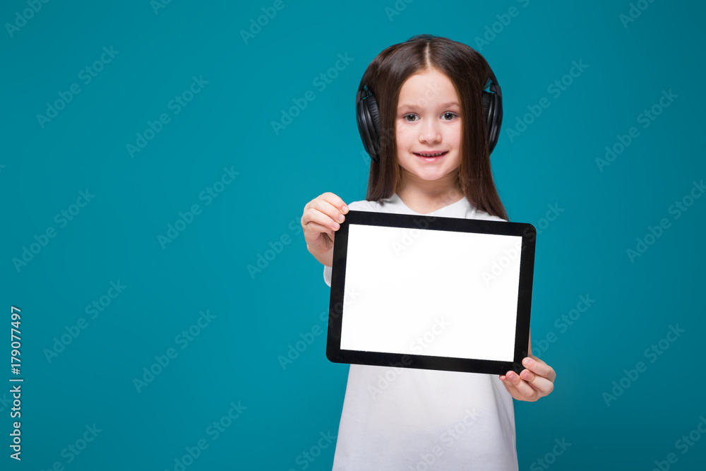 Beauty little girl in tee shirt and earphones with long hair hold tablet Beauty little girl in tee shirt and earphones with long hair hold tablet