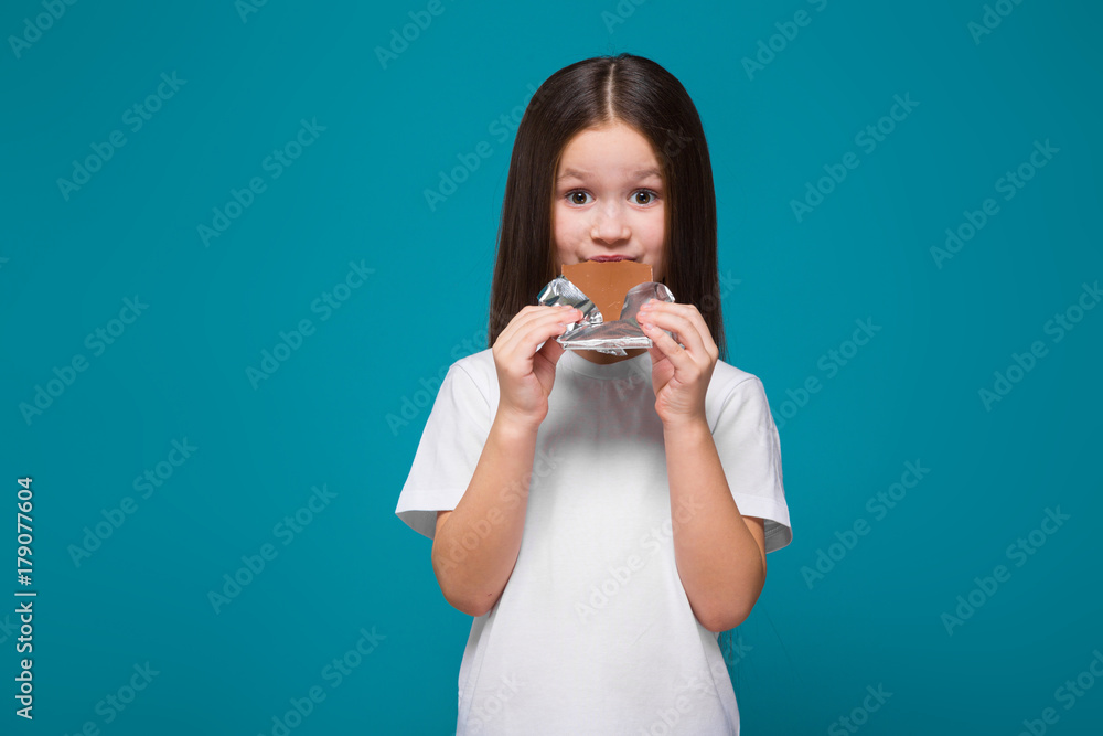 Cute little girl in tee shirt with long hair, with candy bar in hands Cute little girl in tee shirt with long hair, with candy bar in hands