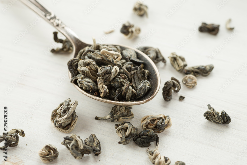 Dry tea in a metal spoon on a white wooden table