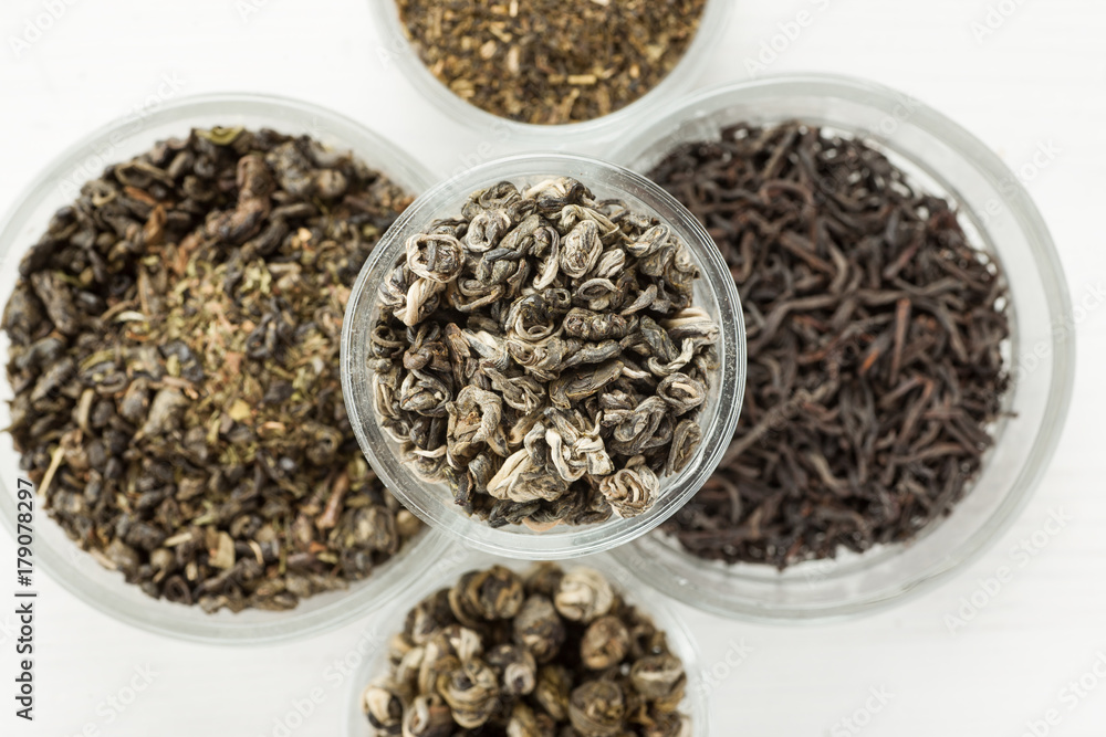 Different dry tea in a small glass dishes on a white wooden table Different dry tea in a small glass dishes on a white wooden table