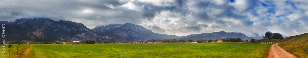Path to the Neuschwanstein castle through the rural meadow with view on Alps mountain