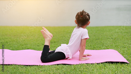 Child girl doing yoga in the public park.