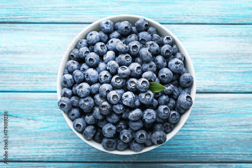 Fotografi Ripe blueberries in bowl on blue wooden table