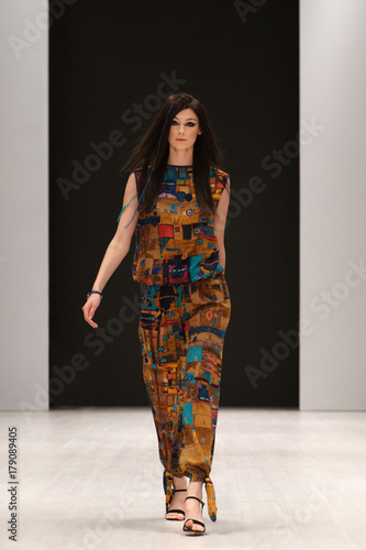 Fotografie Fashion model in silk dress with ethnic ornament walking on podium during fashion week show