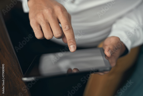 Close-up. Young man working on a tablet. A cafe. Blurred background. White shirt