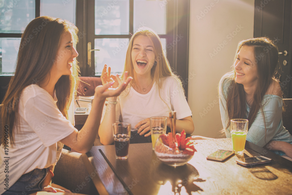 Happy teenage girls talking and laughing in a cafe. - obrazy, fototapety, plakaty 